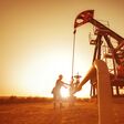 Oil worker is checking the pump near oil derrick on the sunset background.