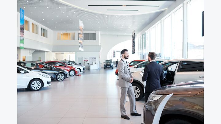 Professional salesperson selling new cars in a modern auto salon. Two men standing and choosing a new car