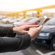 Car sharing service or rental concept. Sharing economy and collaborative consumption. Customer man suit hand using smart phone with blur cars background with fare light effect.