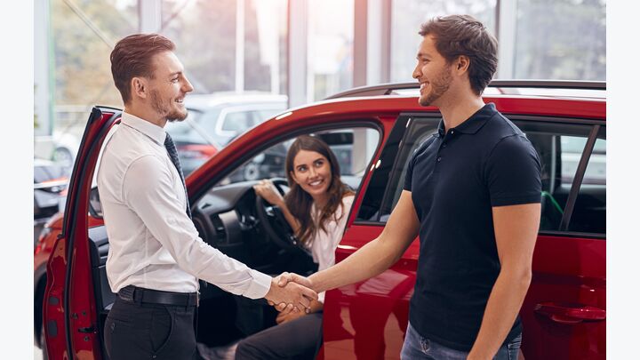 Side view of male dealer and customer smiling and shaking hands in agreement while making deal in modern car dealership