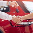 Unrecognizable manager shaking hand of customer and handing keys while sealing deal in car dealership
