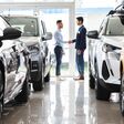 Middle-eastern young man customer and sales assistant shaking hands, car showroom interior, friendly manager greeting wealthy arab guy, standing among luxury brand new autos, full size shot