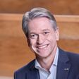 Porträt von Dr. Tim Steiskal Vertriebsleiter Skoda Deutchland im blauen Anzug mit Holz im Hintergrund.