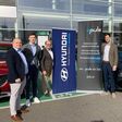 Hyundai und epuls Angestellte und Geschäftsführer vor geparkten Hyundai Autos mit Bannern ihrer betriebe.